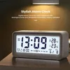 A digital alarm clock is displayed on a wooden surface, with a warm light illuminating the background. Produktbild-Vorschau
