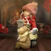 A Christmas-themed figurine of a girl with a lantern and a reindeer in front of a fireplace. Produktbild-Vorschau