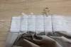 A close-up view of the top edge of a gray curtain with a white heading tape and pleating hooks, on a wooden surface. Produktbild-Vorschau