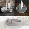 A collage of images showing a round, light gray candle holder with multiple candle holders inside. The candle holder is shown on different backgrounds, including a wooden surface and a marble-like surface. Some images show the candle holder with white cand Produktbild-Vorschau