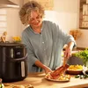 A woman is plating food next to an air fryer in a kitchen. Produktbild-Vorschau