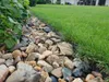 A garden bed edging made of black plastic, separating a rock-filled border from a neatly mowed lawn. Anteprima dell’immagine prodotto
