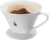 A white ceramic coffee dripper with a filter and coffee grounds inside, shown on a white background. Produktbild-Vorschau