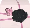 A close-up of a pink perfume box with a butterfly graphic and a black wax seal. Podgląd zdjęcia produktu