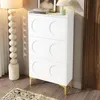A white shoe cabinet with gold legs is shown in a room with a floor lamp and a rug. Anteprima dell’immagine prodotto