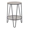 A round, two-tiered side table with a wood-grain top and shelf, supported by black metal hairpin legs, photographed against a white background. Anteprima dell’immagine prodotto