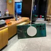 A green smartphone case with a magnetic charging ring is shown hanging in front of a cafe counter. Náhled obrázku produktu