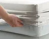 A hand is shown tucking a fitted sheet onto a mattress. Produktbild-Vorschau