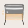A gray baby crib with a white mesh side and an orange highlighted storage area at the bottom. There are also orange arrows indicating adjustability. Náhľad obrázku produktu
