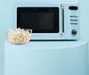 A retro-style blue microwave oven with a bowl of popcorn in front of it, set against a light blue background. Podgląd zdjęcia produktu