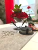 A table setting with a festive Christmas theme, featuring a red flower arrangement in a glass holder on a gray felt table runner. Produktbild-Vorschau