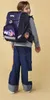 A young girl wearing a backpack and jeans, looking over her shoulder. Produktbild-Vorschau