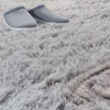 A close-up view of a fluffy gray rug with a pair of gray slippers on it. Produktbild-Vorschau