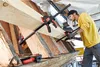 A man is using a clamp to hold wooden beams together. Náhľad obrázku produktu