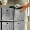 A person is placing a folded garment into a gray fabric storage box, which is part of a stack of similar boxes in a closet. Produktbild-Vorschau