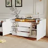 A white and black sideboard with gold accents, featuring open drawers and doors, displaying various decorative items and books. Produktbild-Vorschau