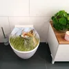 A toilet seat with a fox image is shown in a bathroom setting next to a cabinet with a plant. Produktbild-Vorschau