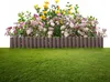 A garden border made of brown wooden-look palisades with flowers and green grass in front. Náhled obrázku produktu