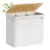 A white laundry basket with a bamboo lid and three compartments, shown with a few bamboo leaves on the side. Produktbild-Vorschau