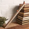 A wooden advent calendar in the shape of stairs with numbered steps, featuring small Christmas figures, placed on a stack of books next to some greenery. Produktbild-Vorschau