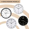 Four different models of MONZANA® wall clocks are displayed against a light brown and white background. Produktbild-Vorschau