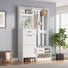 A white entryway organizer with a bench, coat hooks, and storage shelves is shown in a room with a gray wall and a window. Podgląd zdjęcia produktu