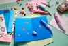 A collection of stationery items, including pens, beads, stickers, and a greeting card, arranged on a light green surface. Anteprima dell’immagine prodotto