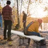 People gathered around a white folding bench in a wooded area with autumn foliage. Produktbild-Vorschau