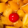 A close-up view of a fruit cocktail with a cherry in the center. Produktbild-Vorschau