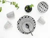 A collection of black and white patterned ceramic dishes and mugs arranged on a white surface with a sprig of greenery. Produktbild-Vorschau