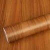 A roll of wood-grain adhesive vinyl wrap is shown on a surface with a similar wood grain pattern. Anteprima dell’immagine prodotto