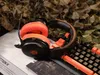 A gaming headset and keyboard are placed on a surface with a camouflage net in the background. Anteprima dell’immagine prodotto
