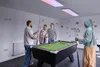 Four people are playing pool in a room with colorful decorations on the wall and modern lighting fixtures. Produktbild-Vorschau