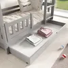 A close-up view of a bunk bed's lower section, showing a pull-out drawer with folded clothes and two small balls on the floor. Produktbild-Vorschau