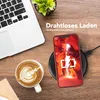 A smartphone is wirelessly charging on a charging pad next to a laptop and a cup of coffee. Produktbild-Vorschau