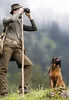 A man with binoculars and a dog in a natural setting. Anteprima dell’immagine prodotto