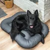 A black dog is lying on a gray dog bed on a wooden floor. Produktbild-Vorschau