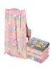 A pink unicorn-patterned blanket draped over a chair, with a stack of folded blankets in front of it. Anteprima dell’immagine prodotto