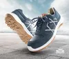 Two blue work shoes are shown in a dynamic pose against a sky and concrete background. Produktbild-Vorschau