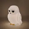 A white owl-shaped lamp with yellow eyes and black markings on its wings, sitting on a light gray surface. Anteprima dell’immagine prodotto