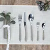 A set of cutlery arranged on a placemat on a wooden table, with a decorative sprig of greenery and berries. Podgląd zdjęcia produktu