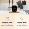 A black mini rice cooker is shown on a cutting board on a kitchen counter, with kitchen utensils hanging in the background. The bottom half of the image contains text and icons highlighting features. Produktbild-Vorschau