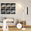 A living room scene with a floor lamp, sofa, and coffee table. A hand is holding a remote control. Náhľad obrázku produktu