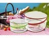 A picnic scene with food items covered by mesh food covers. Produktbild-Vorschau