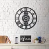 A black metal gear clock hangs on a white brick wall above a desk with a laptop, books, and decorative items. Náhľad obrázku produktu