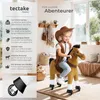 A young girl dressed as a cowboy rides a toy horse in a living room. Náhled obrázku produktu