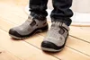A person wearing dark blue jeans and gray work shoes stands on a wooden floor. Produktbild-Vorschau