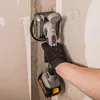 A person's hand wearing a black glove is holding a tile vibrator tool against a wall. Podgląd zdjęcia produktu