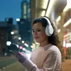 A woman wearing headphones is looking at her phone at night in a city. Voir les images du produit
