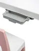 A close-up view of a small gray drawer attached to a white desk, with the top of a pink chair visible below. Produktbild-Vorschau
